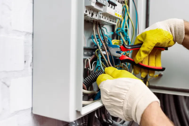Električar z orodjem popravlja električno napeljavo v električni omarici.