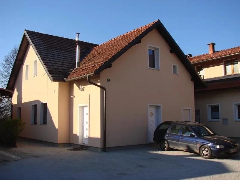 Prenovljena fasada marelične barve na enodružinski hiši v Osrednji Sloveniji. Pred hišo je parkiran avtomobil.