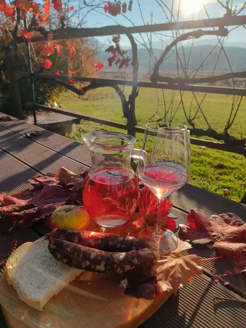 Vrč in kozarec vina, ki so ga pridelali vinogradniki na območju Slovenskih Konjic. Ob vinu je tudi pogostitev s hrano.