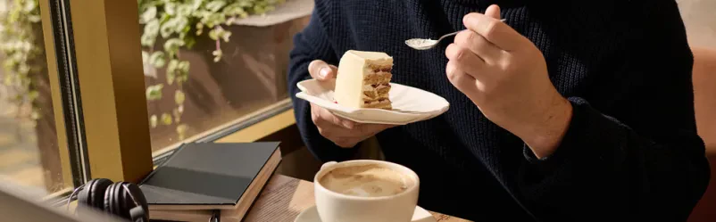 Gostja v kavarni uživa v okusni tortici, postreženi ob sveže pripravljeni kavi.