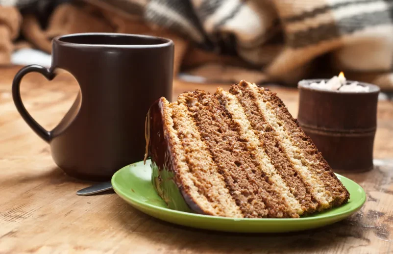 Kos torte na krožniku na mizi lokala, poleg je skodelica sveže pripravljene kave.