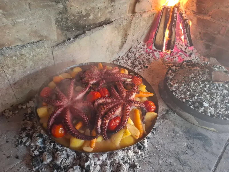 Hobotnica in krompir, ki se peče v posodi nad žerjavico. Del ponudbe cateringa za praznovanja v Osrednji Sloveniji.