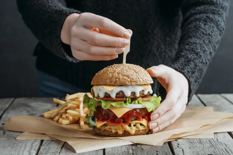 Roke z velikim okusnim cheeseburgerjem in pomfrijem