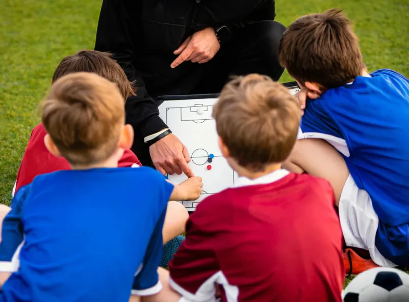 Trening ravnotežja z nogometno opremo Mlad nogometaš izvaja vaje za ravnotežje na posebni blazini na travnatem igrišču, kar je ključen del nogometnih priprav tekmovalcev za izboljšanje stabilnosti.