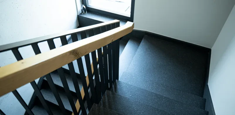 Prenovljeno stopnišče v črni barvi z lesenimi detajli na ograji.