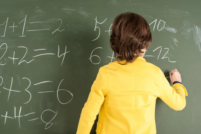 Otrok pred tablo rešuje matematični problem v šoli.