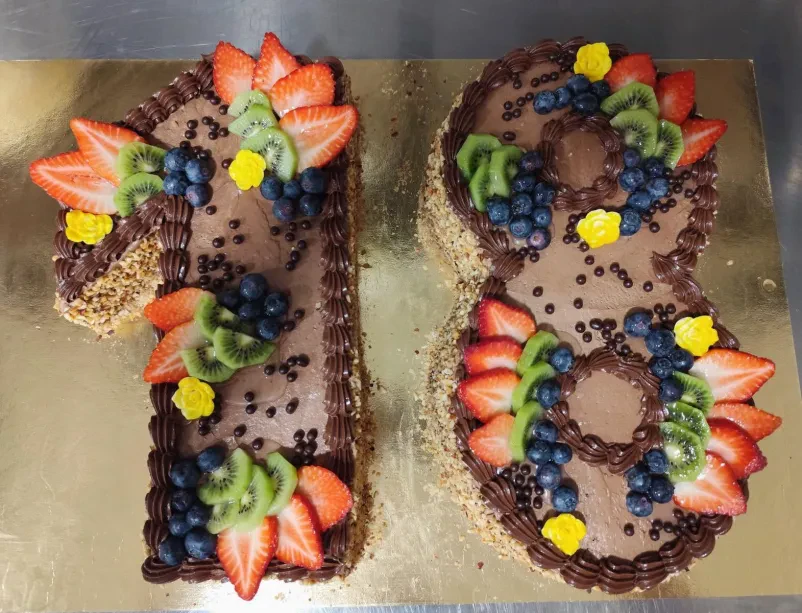 Čokoladna torta v obliki številke 18, obložena z jagodami, kivijem, borovnicami, čokoladnimi mrvicami in rumenimi okrasnimi rožicami