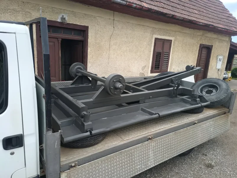 Peskanje kovinskih konstrukcij na gradbišču Delavec v polni zaščitni opremi peska velike kovinske strukture na zunanjem gradbišču. Poudarek je na varnosti in učinkovitosti dela.