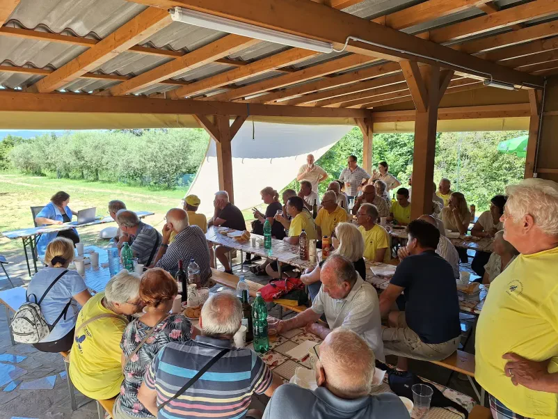 Člani društva čebelarjev sedijo za mizami na terasi in poslušajo predavanje v sklopu izobraževanja čebelarjev v Kopru.