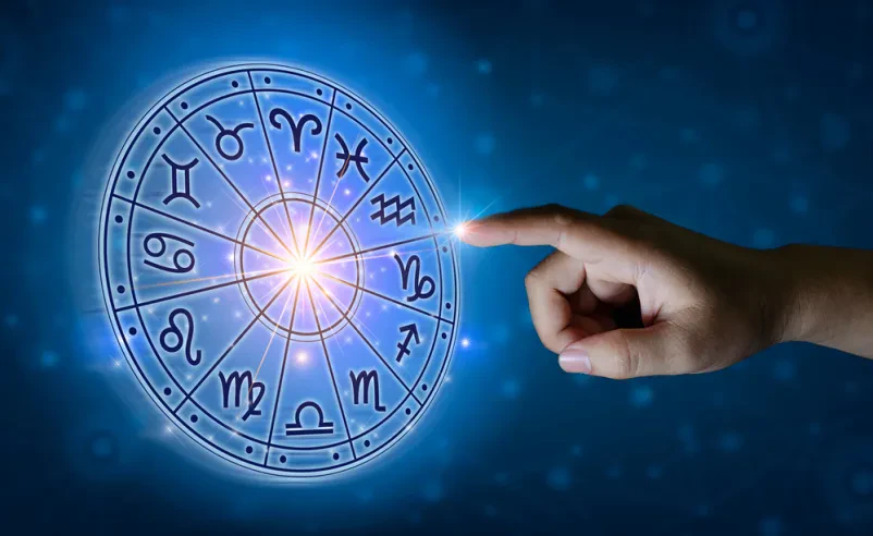 Astrološka znamenja na nebu, roka s prstom kaže na določeno znamenje, v ozadju je zvezdnato nebo.