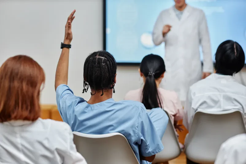 Dijak dviguje roko, ko doktor profesor sprašuje vprašanje v učilnici, polni dijakov