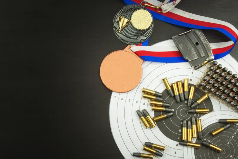 Medalje, tarča in naboji, ki predstavljajo uspešno tekmovanje v športnem streljanju.