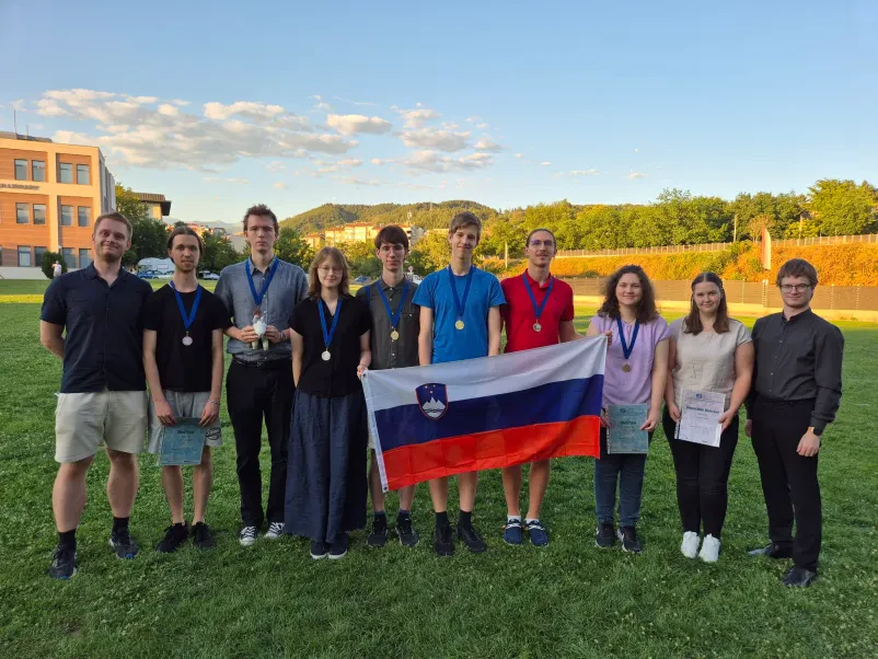 Študentje fizike na dogodku v naravi na katerem v rokah držijo slovensko zastavo.