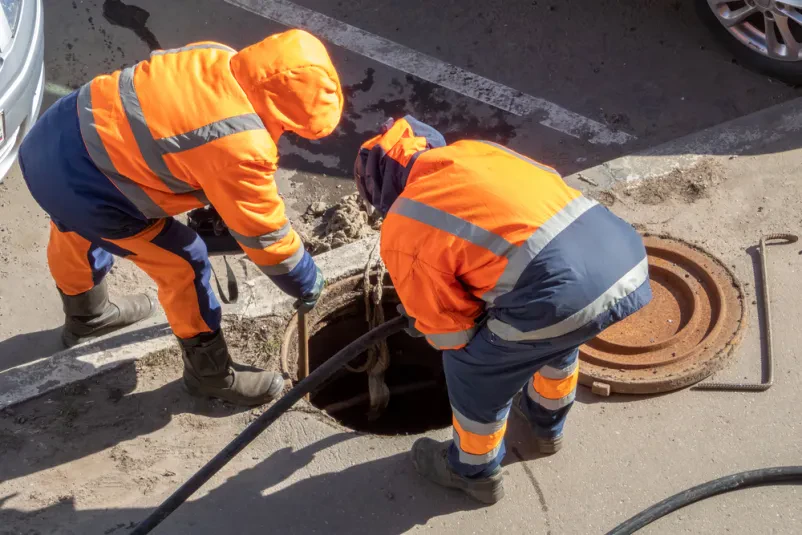 Delavca v oranžni zaščitni obleki opravljata vzdrževanje cestišča in praznjenje odtokov na Pohorju.
