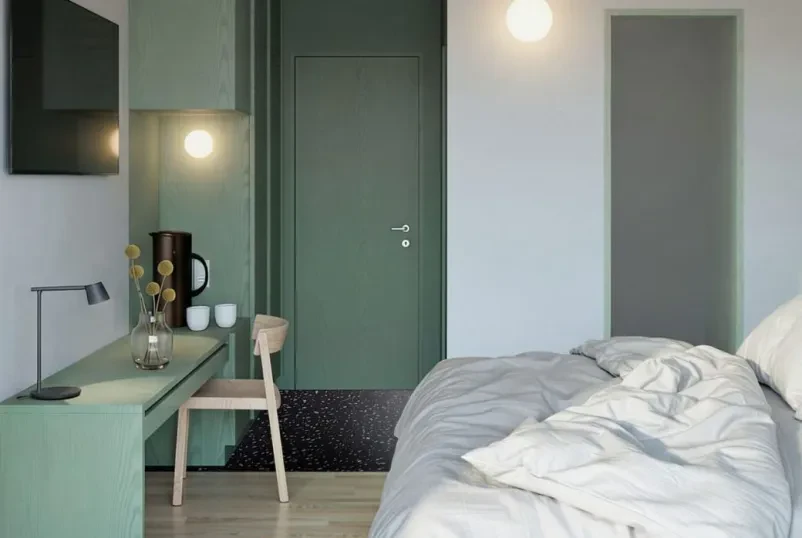 Hotelska soba s posteljo, mizo, stolom in televizijo, soba je opremljena v naravnih in zelenih barvah.