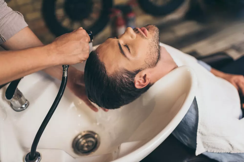 Frizerka umiva lase moškega v frizerskem salonu