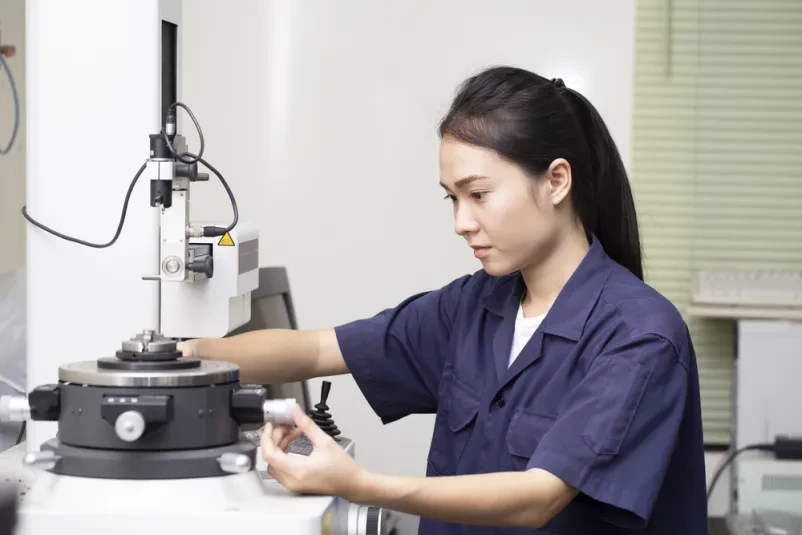 Inženirka testira strojno opremo Mlada inženirka azijskega porekla v industrijskem laboratoriju testira in nastavlja kompleksno strojno opremo, kar kaže na zagotavljanje skladnosti izdelkov.