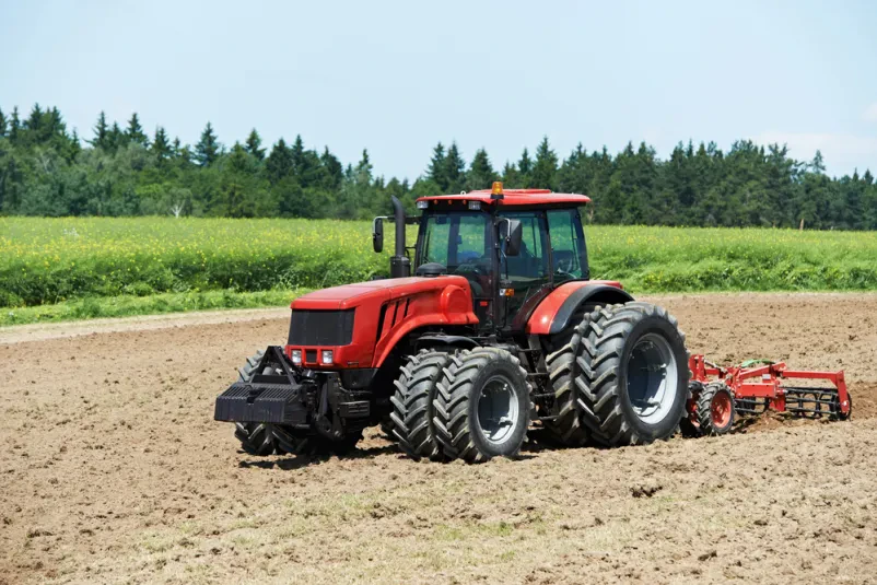 Oranje njive s težkim kmetijskim traktorjem Masiven traktor z robustnim plugom temeljito obdeluje polje, dvigajoč svežo prst. Priprava tal je ključno kmetijsko delo za uspešno sezono.