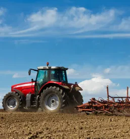 Zmogljiv rdeč traktor z večbrazdnim plugom obdeluje polje, pripravlja zemljo za sajenje. Takšna dela s traktorjem so ključna za kmetijstvo v Mavčičah.