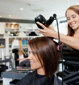 Frizerka s krtačo in sušilcem spretno suši lase stranke. Za popolno urejanje pričeske, dober frizerski salon Logatec.
