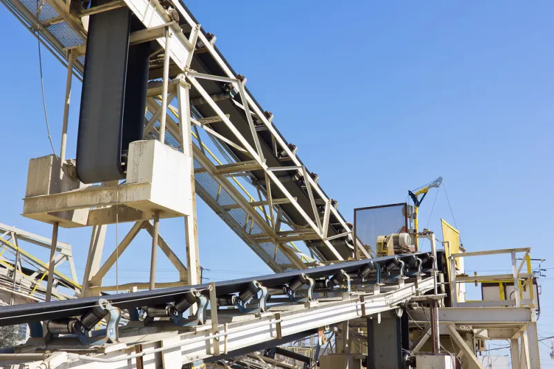 Transportni trak v obratu za beton Dolgi transportni trak za prevoz peska in gramoza se razprostira na prostem. Ta vitalni del opreme je ključen pri učinkoviti izdelavi betona in betonskih mešanic.