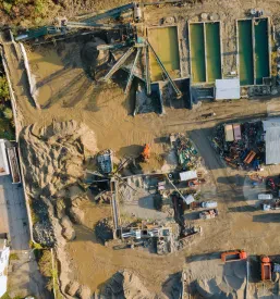 Širok pogled na industrijsko cono, kjer se nahaja tovarna za proizvodnjo penobetonskih blokov. Vidni so visoki stolpi in skladišča, ki so del kompleksnega proizvodnega procesa.