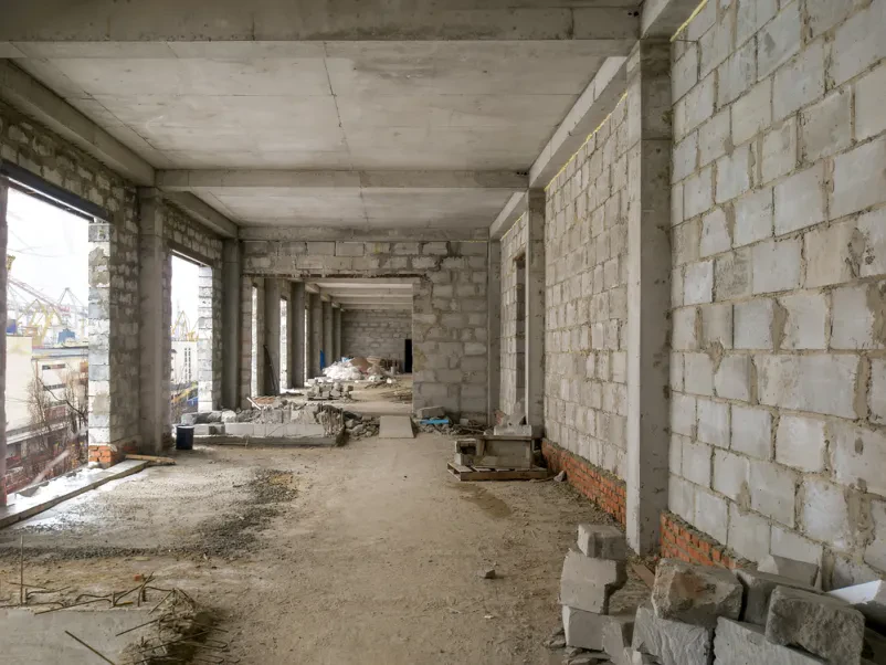 Pogled v notranjost nedokončane stavbe z odprtimi betonskimi stenami in stropi, ki pričajo o začetni fazi gradbenih del.