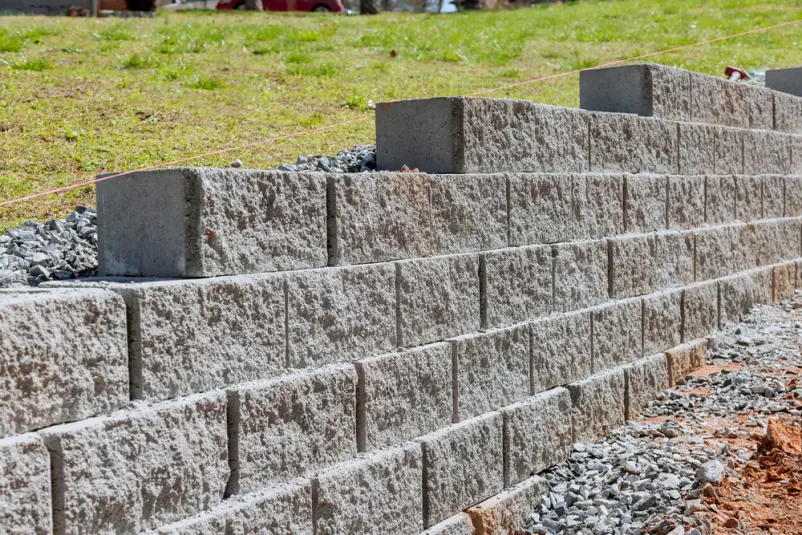 Gradnja opornega zidu iz betonskih blokov Gradbeni delavci skrbno postavljajo betonske bloke za oporni zid, ki bo služil kot zaščita in opora na terenu ob novogradnji. Prikazana je faza, ko je zid že delno postavljen, kar kaže na potek Izdelava manjših škarp Ljubljana, Goriška.