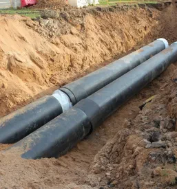 Položene cevi za vodo v globokem jarku na sončen dan, pripravljene za vgradnjo kot del infrastrukture.