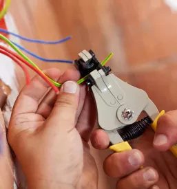 Električarjeve roke s kleščami skrbno luščijo izolacijo z bakrenih žic, kar je pomemben korak pri novih elektroinštalacijah, ki zagotavljajo varnost in učinkovitost.