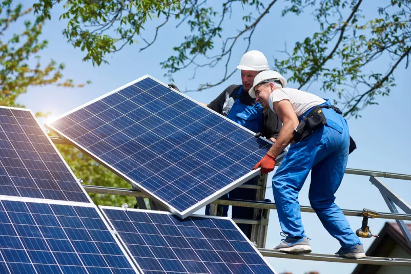 Dva tehnika montirata težek fotovoltaični panel Dva tehnika montirata velik fotovoltaični panel. Ključen del montaže sončnih elektrarn Slovenija, ki zahteva natančno in varno postavitev na jekleno ploščad.