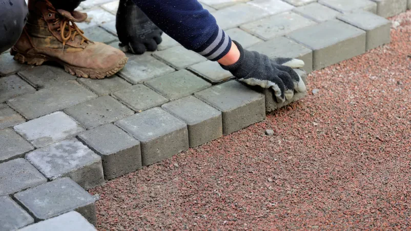 Delavec polaga betonske tlakovce na gramoz Delavec s skrbnostjo polaga betonske tlakovce na utrjen gramoz, ustvarjajoč trdno in estetsko površino. Takšno polaganje tlakovcev Logatec zagotavlja dolgotrajno rešitev za dovoze in poti.