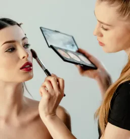Lepa vizažistka s čopičem nežno nanaša korektor na obraz privlačnega modela med studijskim fotografiranjem.