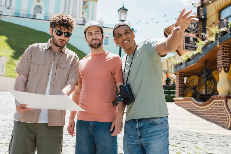Afriško-ameriški turist s fotoaparatom kaže v daljavo, vodič in prijatelj pa pregledujeta mestni zemljevid.