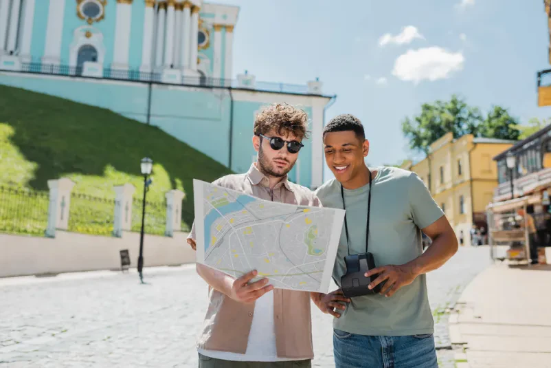 Vodič v sončnih očalih in afriško-ameriški popotnik skupaj preučujeta mestni zemljevid za orientacijo.