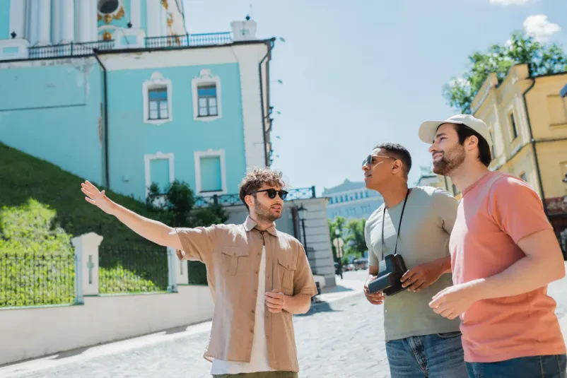 Turistični vodič z roko kaže na zanimivost v mestu, medtem ko bradati moški in afriško-ameriški turist opazujeta.