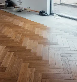 Mojster natančno polaga parket v elegantnem vzorcu ribje kosti v notranjosti doma, kar ustvarja klasičen videz.