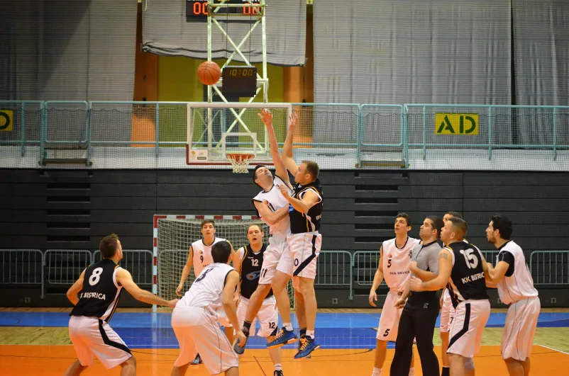 Mladi košarkar na tekmi meče prosti met Mladi igralec izvaja prosti met med intenzivno košarkarsko tekmo, kar kaže na dinamiko športa. Vpis v košarkarski klub Slovenska Bistrica je odprt.