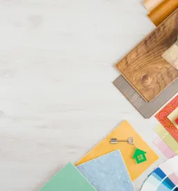 Orodje in materiali, kot so ploščice, meter in ključi, razporejeni na leseni površini, prikazujejo obsežnost projektov.