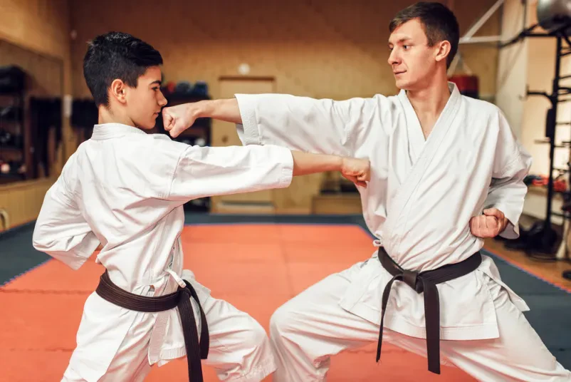 Dva mojstra karata v belih kimonih s črnimi pasovi trenirata v telovadnici. Odličen prikaz za klub Borilne veščine Ljubljana Jarše.