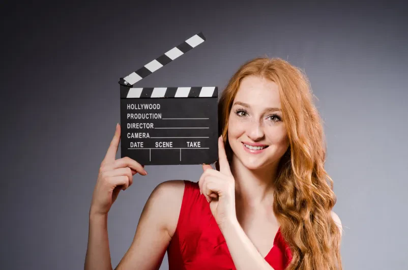 Ženska v rdeči obleki s filmsko klapo Privlačna ženska v rdeči obleki drži odprto filmsko klapo, pripravljena na začetek snemanja.