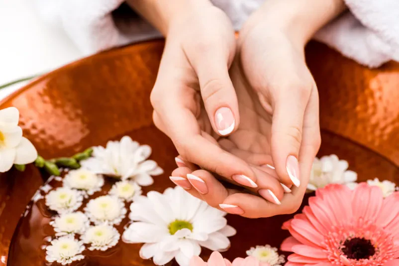 Sproščujoča spa nega rok s cvetjem Ženska uživa v sproščujoči spa negi rok v kozmetičnem salonu, kjer so v vodi cvetovi, kar poudarja naravno lepoto in skrb za kožo.