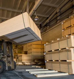 Viličar spretno nalaga velike svežnje lesenih plošč v proizvodnem obratu, kar zagotavlja učinkovito pretovarjanje in skladiščenje materiala.