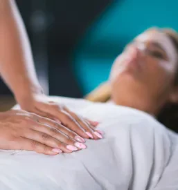 Ženska terapevtka izvaja reiki terapijo z rokami nad ženskim trebuhom, kar prispeva k zmanjšanju stresa in globoki sprostitvi.