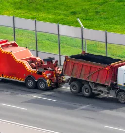 Močan vlečni tovornjak vleče okvarjen tovornjak s prikolico po mestni avtocesti, kar kaže na zmogljivost vlečne službe.