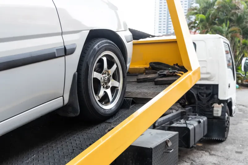 Nalaganje vozila na avtovleko Pokvarjen avtomobil se s pomočjo vitla in kabla nalaga na ploščad avtovleke, pripravljen za varen transport v avtoservis.
