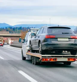 Vlečno vozilo s pokvarjenim avtomobilom na ploščadi vozi po avtocesti, kar ponazarja zanesljivo vlečno službo za vozila v okvari.