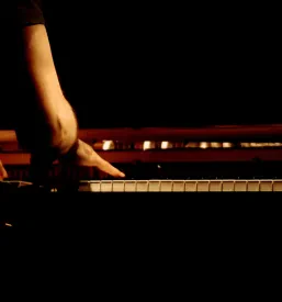 Topel posnetek moškega pianista, ki strastno igra na klavir, z osvetljenimi tipkami, kar poudarja umetniško ustvarjanje.