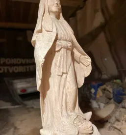 Visoka lesena skulptura Device Marije, izklesana z izjemno natančnostjo, poudarja detajle oblačil in obraza svetnice.