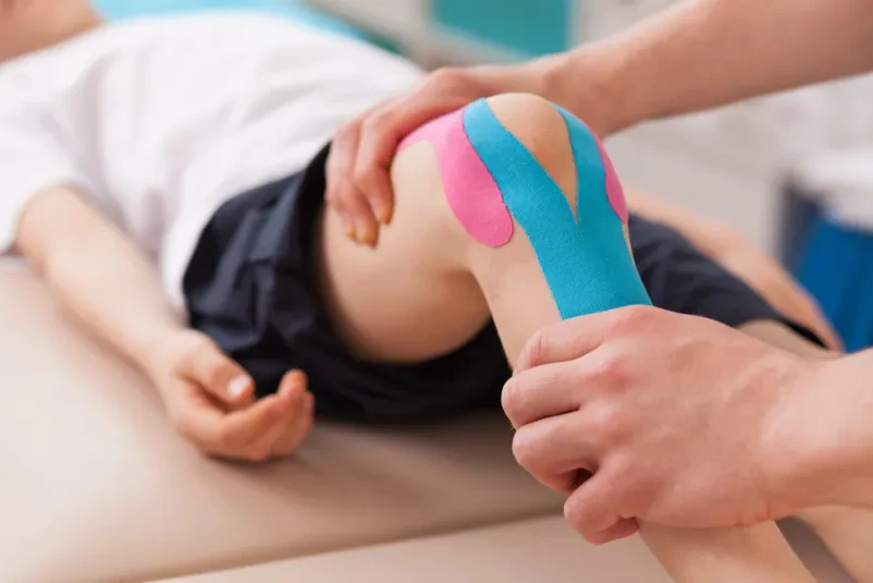 Fizioterapevtka in otrok pri vaji za koleno Fizioterapevtka z otrokom izvaja vajo za koleno. To je del Kvalitetna kineziološka vadba Ljubljana, okolica, ki podpira rehabilitacijo.